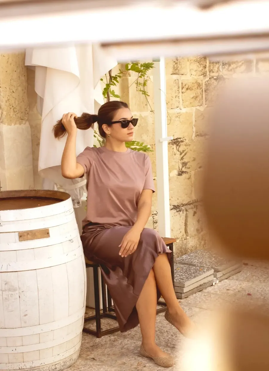 Foto del lookbook di Mati Shop: t-shirt malva e gonna in raso appoggiate a un muro di pietra a Lecce